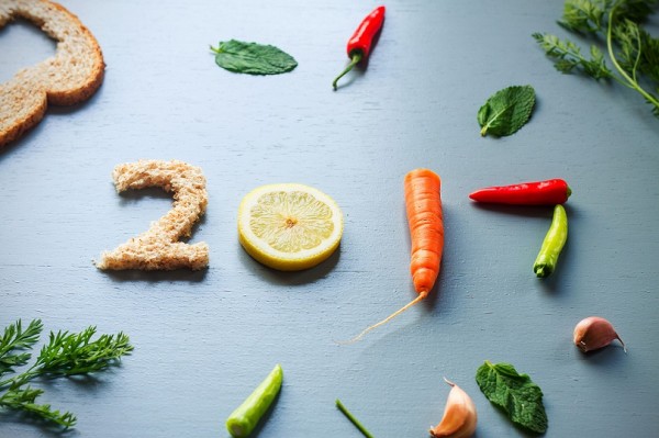 A food preparation on light blue rustic wooden table showing number 2017, old bread, chillies, carrots, peppermint, cloves of garlic, lemon, number 2017, new year letter, overhead shot
